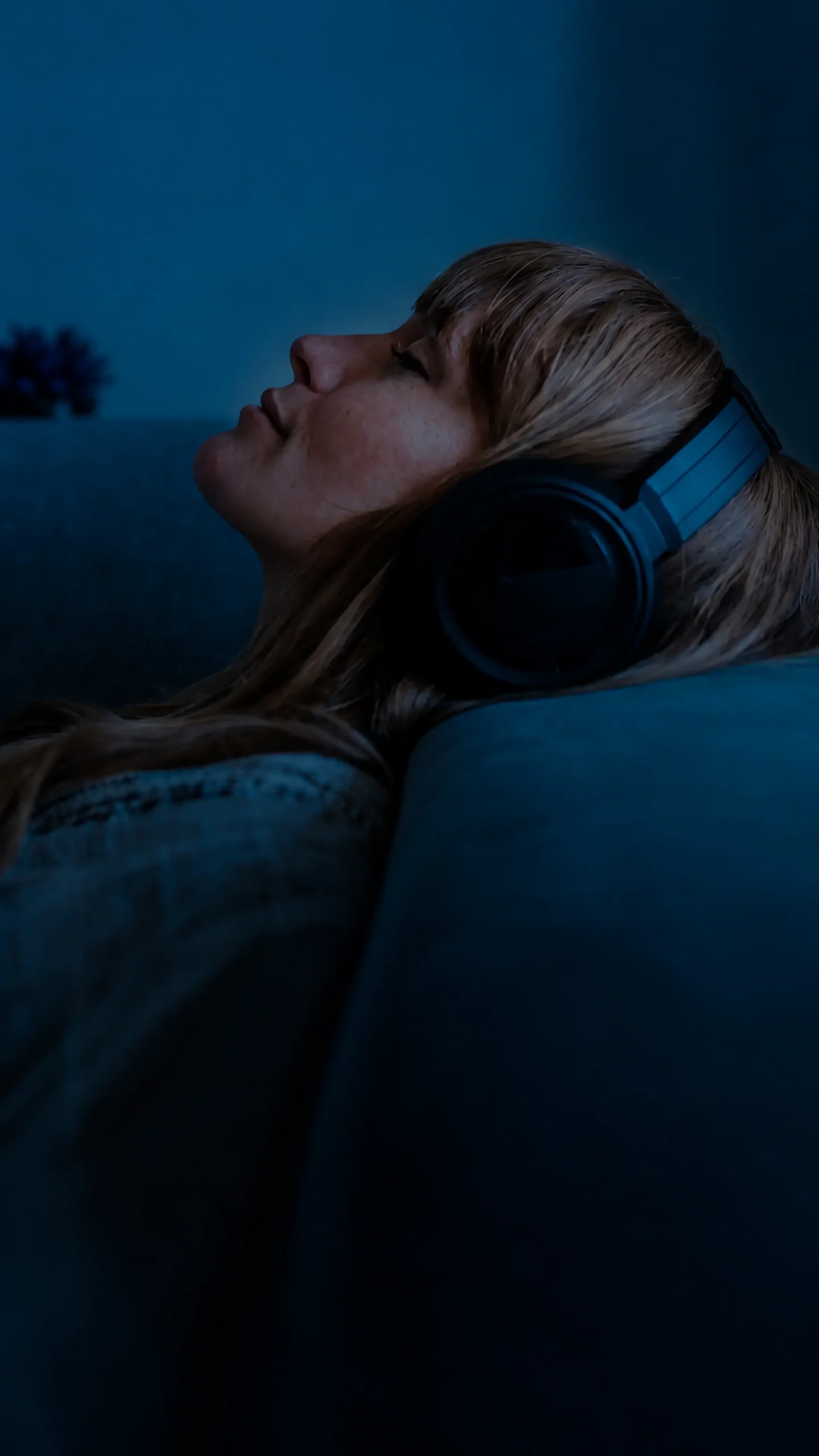 Mujer recostada con los ojos cerrados y audífonos en un ambiente nocturno.